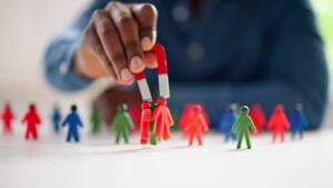 Main tenant un aimant en forme de fer à cheval attirant des figurines rouges parmi des figurines en plastique multicolores.